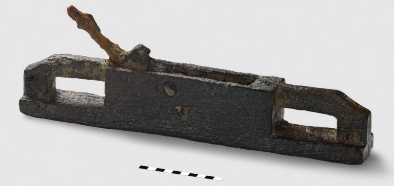 The fully preserved plane is made from a single piece of wood and features an inset iron blade. It is 41 cm long, 7 cm wide, and 5 cm high.